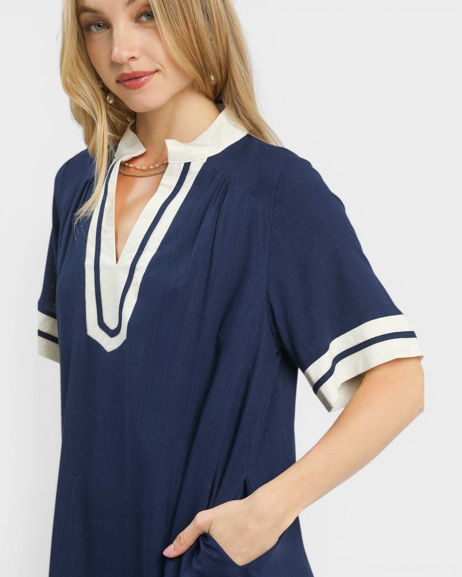 Woman wearing a navy blue dress with white trim on a plain background