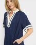 Woman wearing a navy blue dress with white trim on a plain background