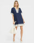 Woman wearing a navy dress with white trim holding a white handbag on a white background