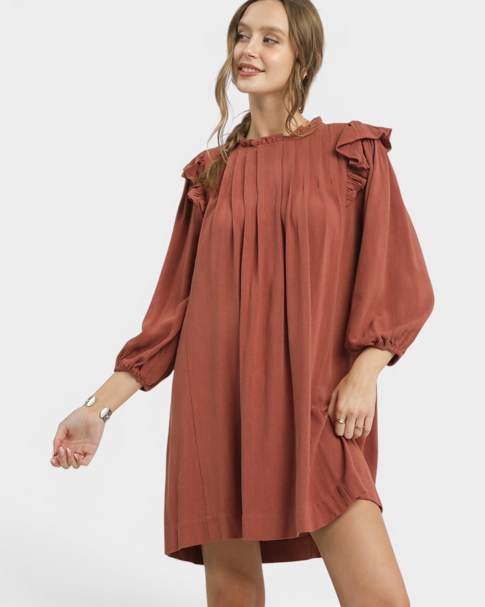 Woman wearing a rust-colored dress with ruffled sleeves on a white background