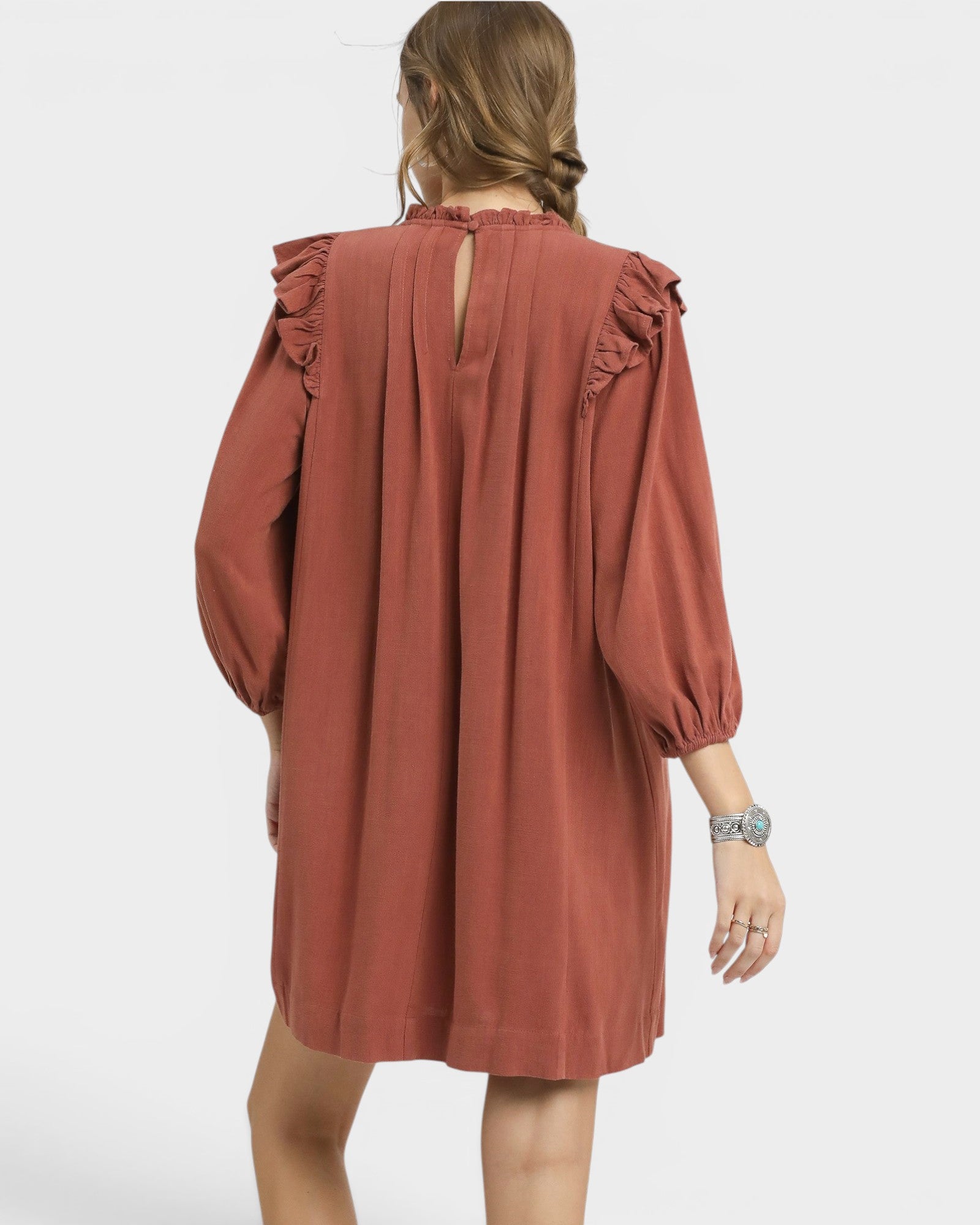 Person wearing a rust-colored dress with ruffled sleeves on a white background