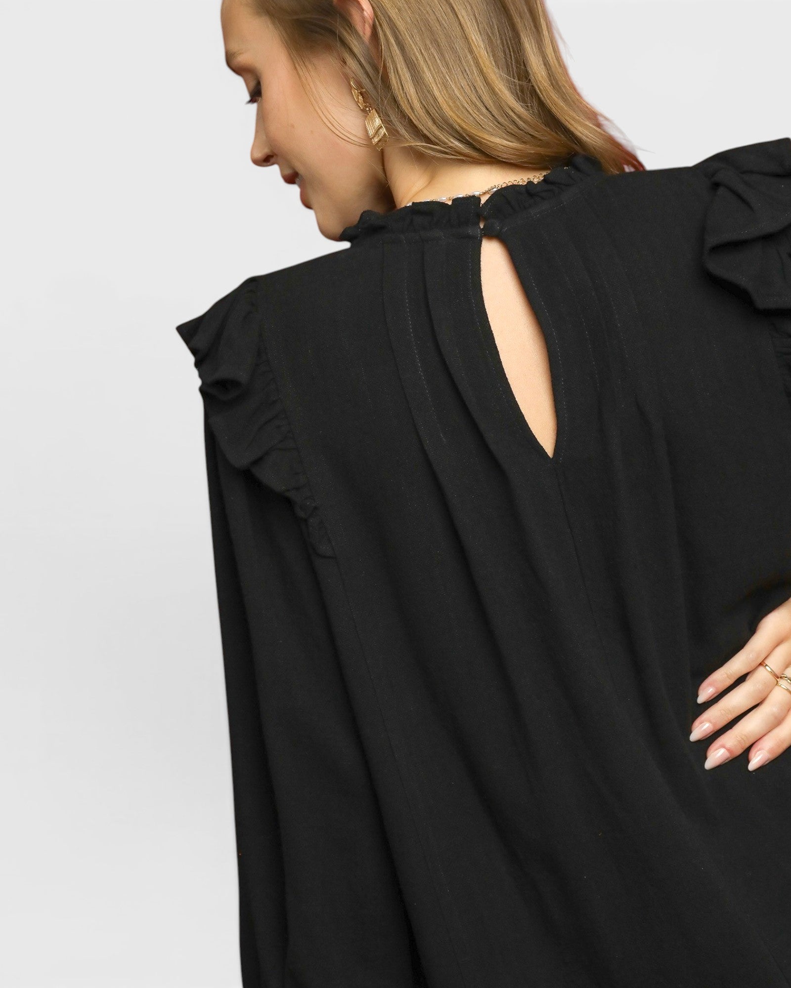 Black blouse with ruffled sleeves worn by a person on a light gray background