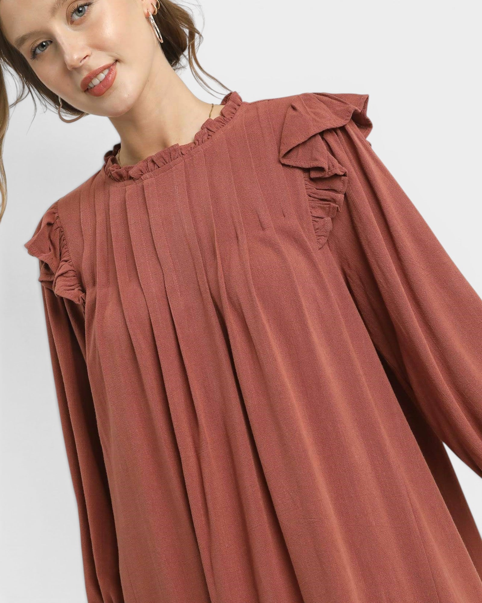 Woman wearing a rust-colored dress with ruffled sleeves on a white background