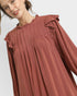 Woman wearing a rust-colored dress with ruffled sleeves on a white background