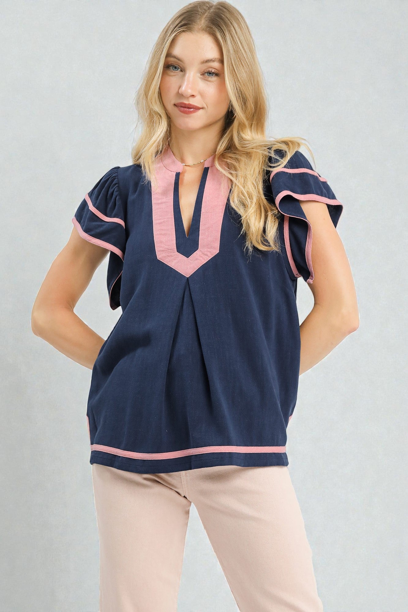 Woman wearing a navy blouse with pink accents on a gray background