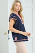 Woman wearing a navy blue top with pink accents in a neutral setting