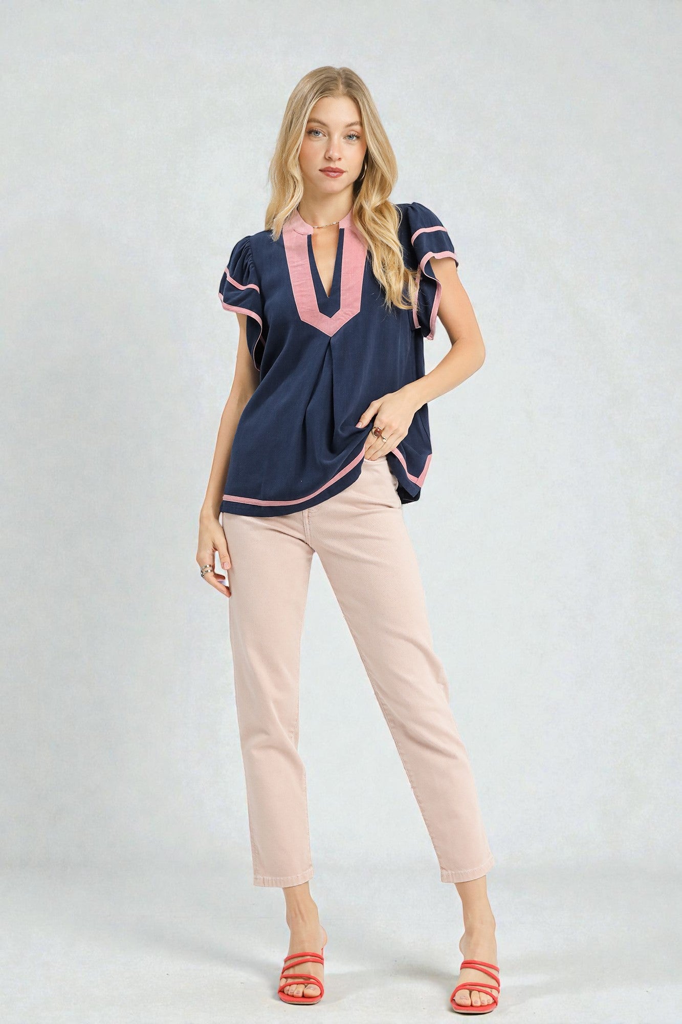 Woman wearing a navy blue top with pink accents and beige pants on a white background
