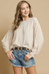 Woman wearing a beige blouse and denim shorts with a chain belt on a beige background