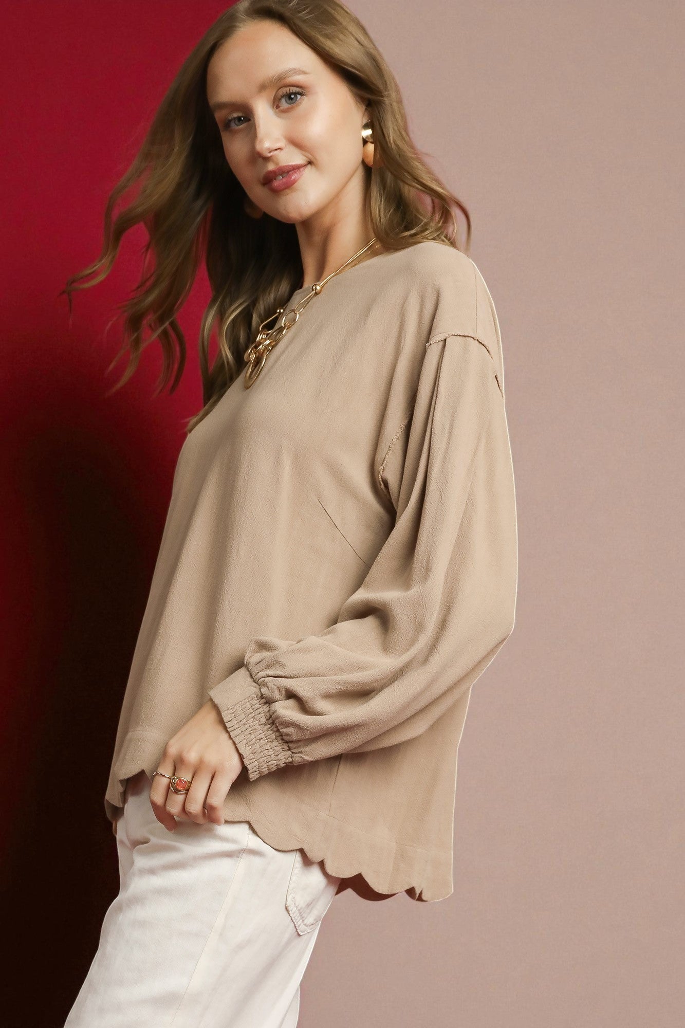 Woman wearing a beige blouse with scalloped edges on a gradient background