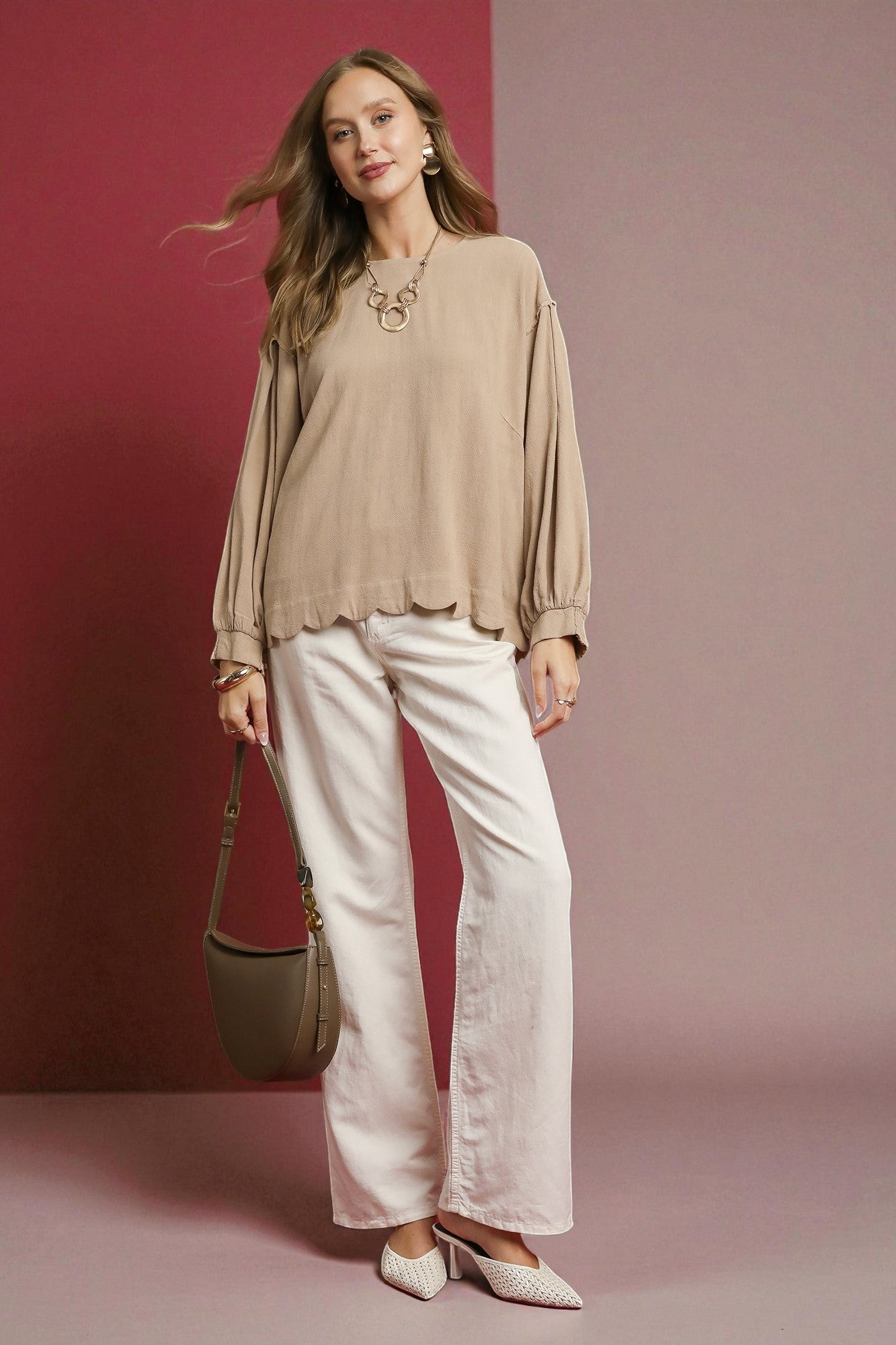 Woman wearing a beige blouse and white pants against a pink background