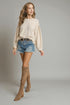 Woman wearing a beige sweater, denim shorts, and tan knee-high boots on a gray background