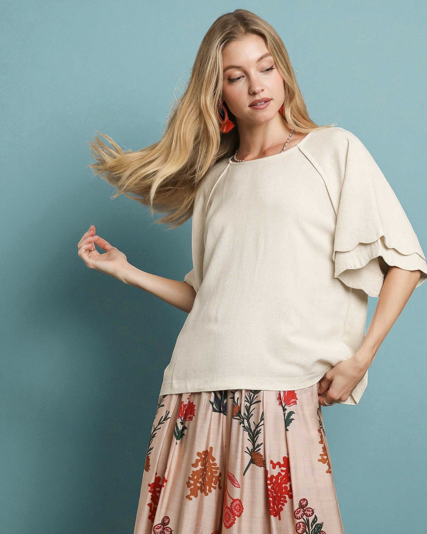 Woman wearing a beige top and floral skirt against a blue background