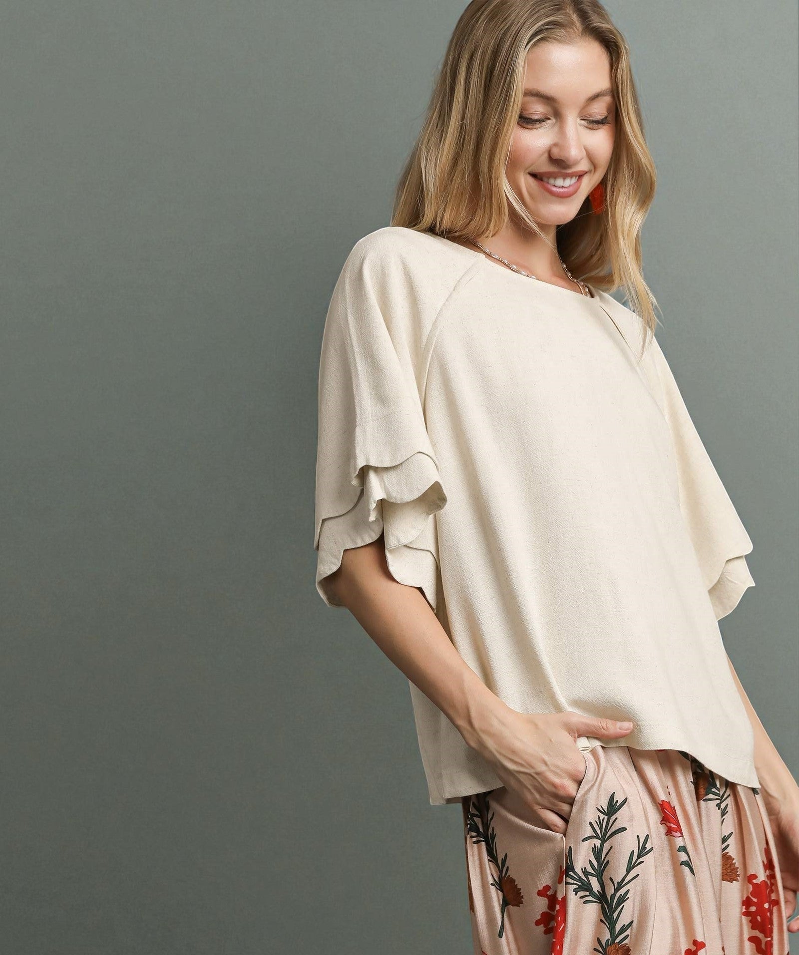Woman wearing a beige top and patterned pants against a gray background