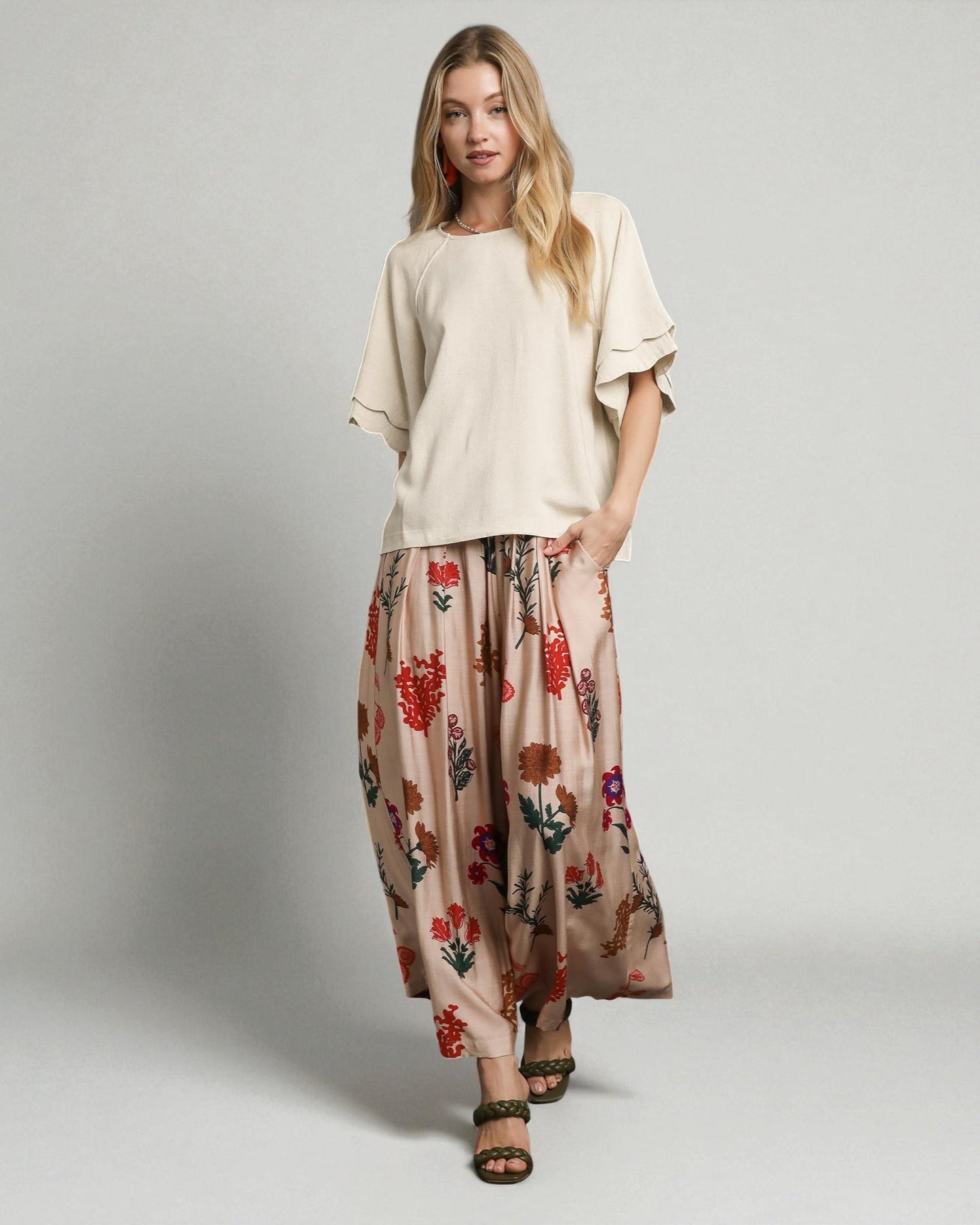 Woman wearing a beige top and floral pants on a plain background