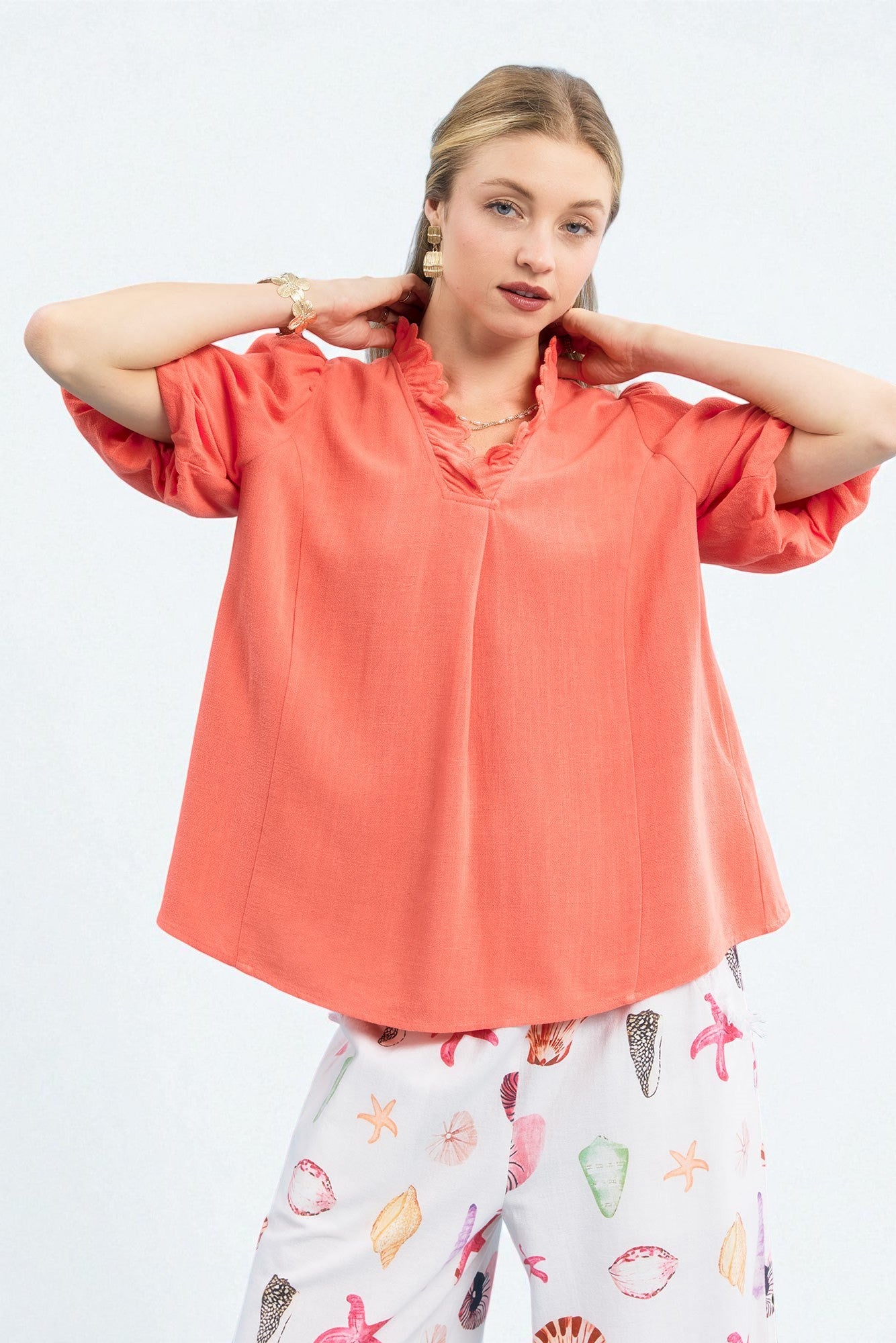 Woman wearing a coral blouse and patterned pants on a white background