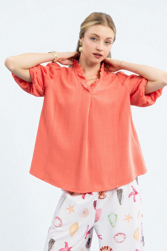 Woman wearing a coral blouse and patterned pants on a white background