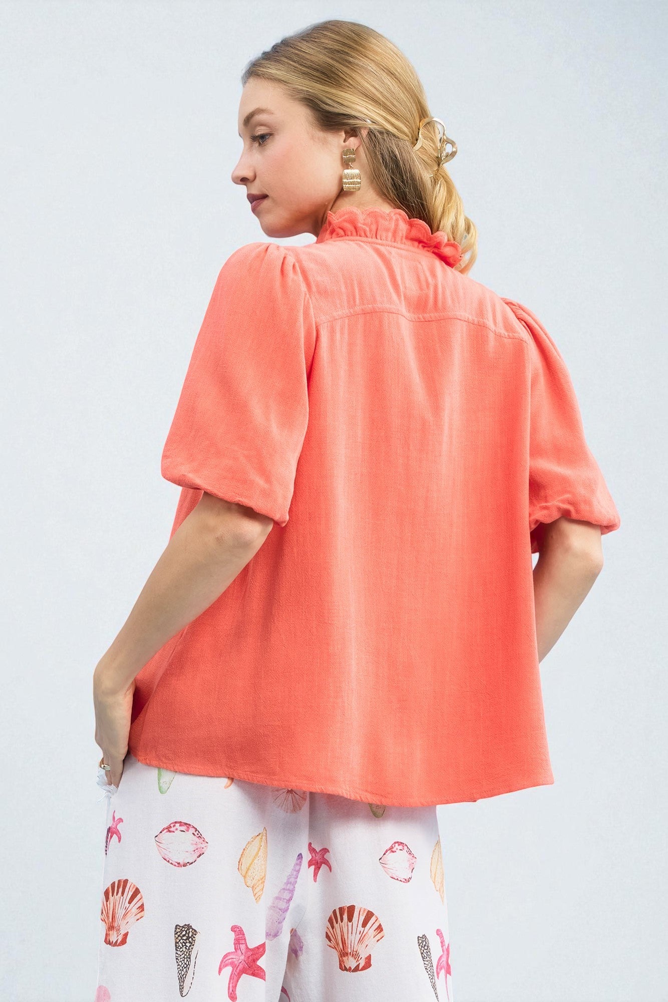 Woman wearing a coral blouse with a white skirt featuring shell patterns on a light gray background