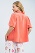 Woman wearing a coral blouse with a white skirt featuring shell patterns on a light gray background
