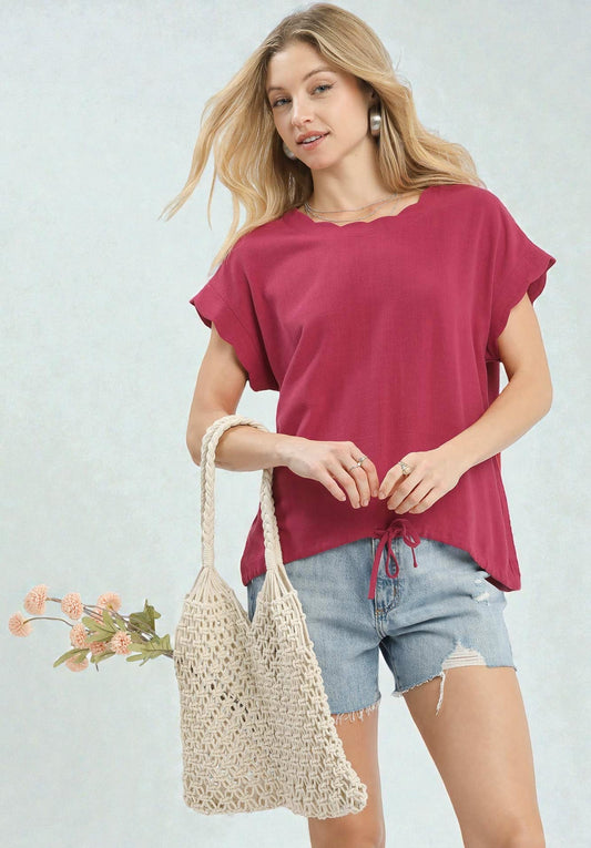 Woman wearing a red top and denim shorts, holding a woven bag with a light gray background