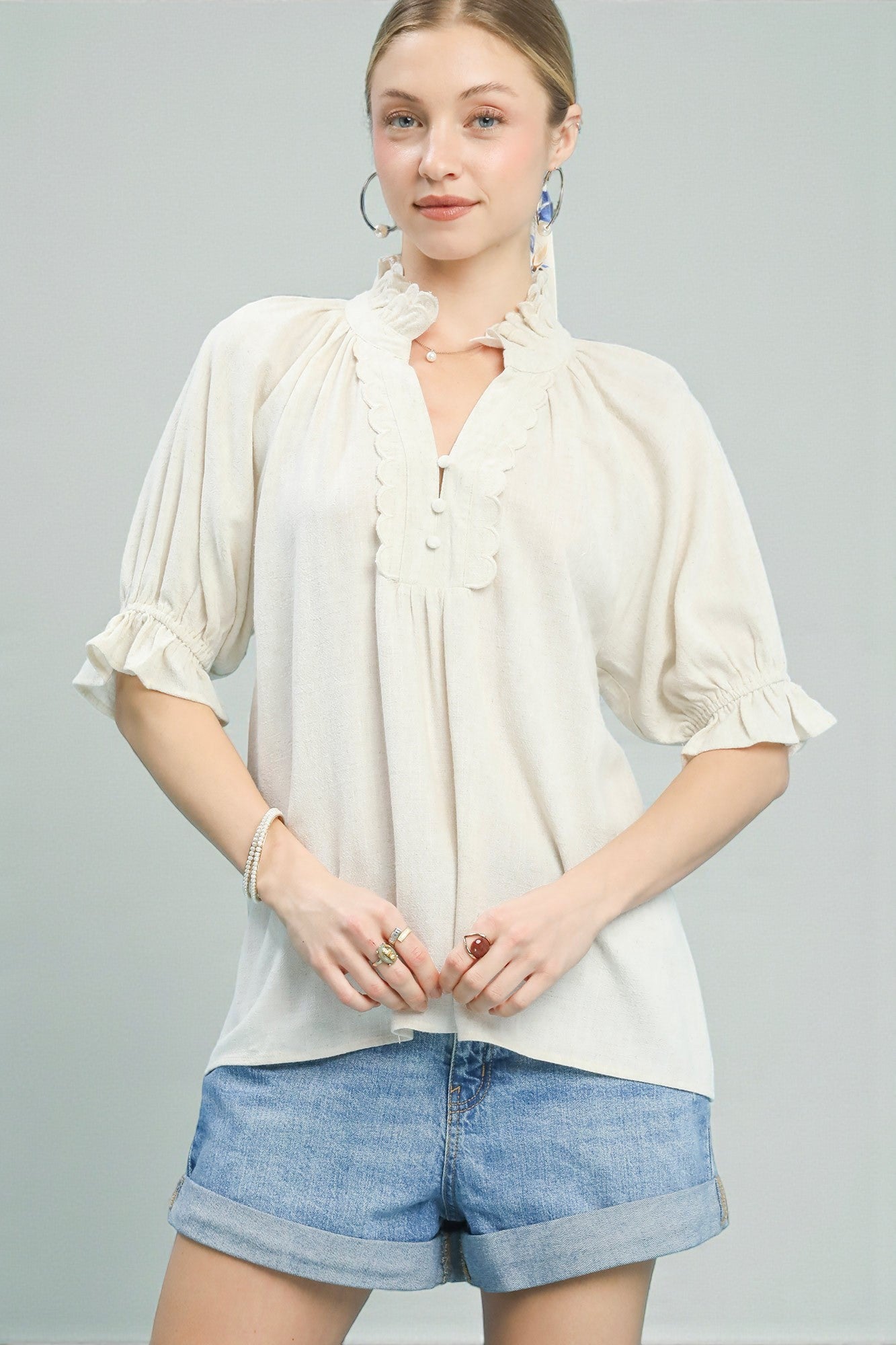 Woman wearing a white blouse with ruffled sleeves and denim shorts on a gray background