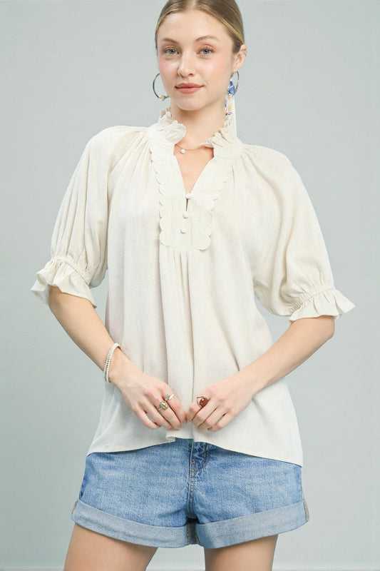 Woman wearing a white blouse with ruffled sleeves and denim shorts on a gray background