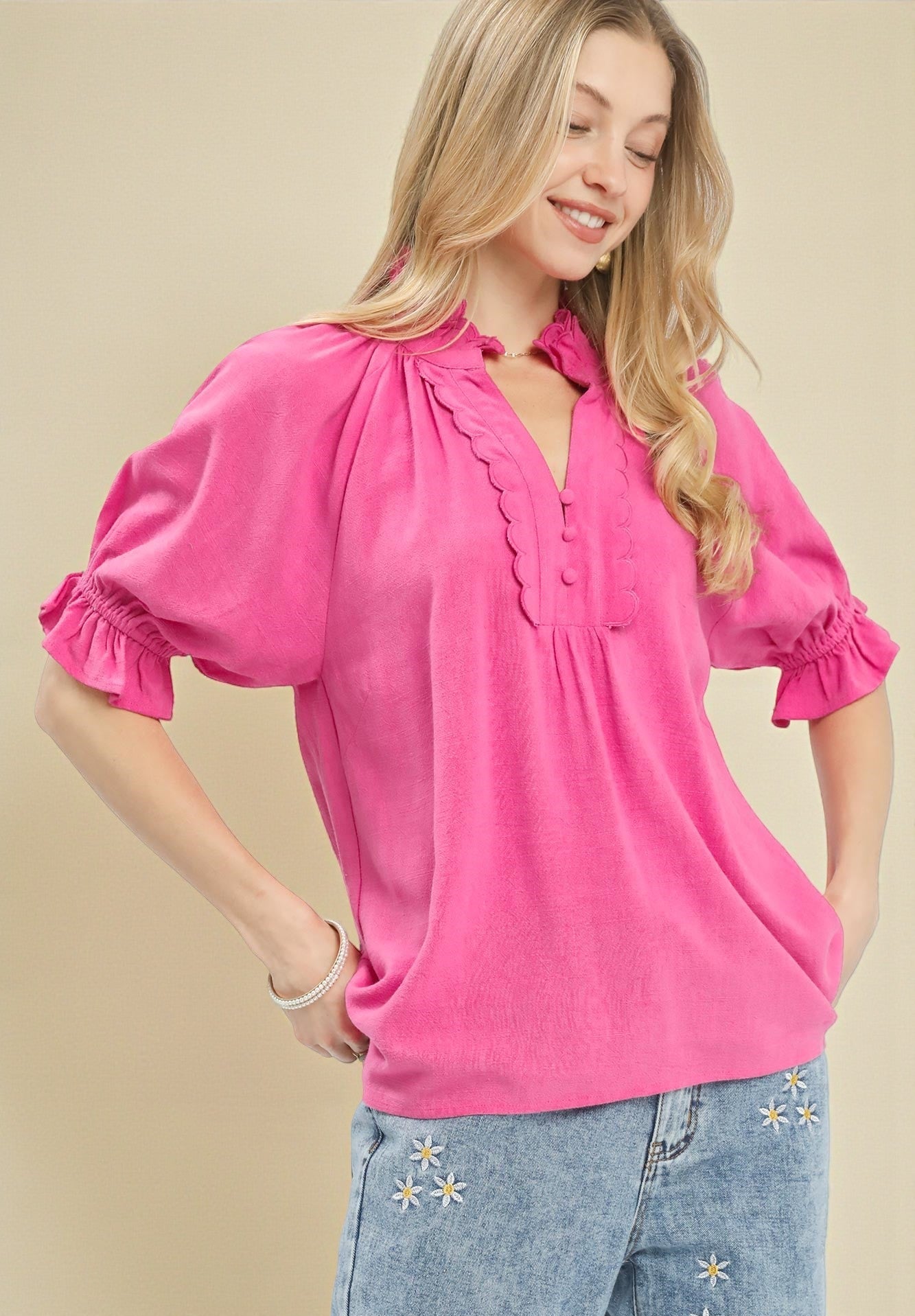 Woman wearing a bright pink blouse with ruffled details on a beige background