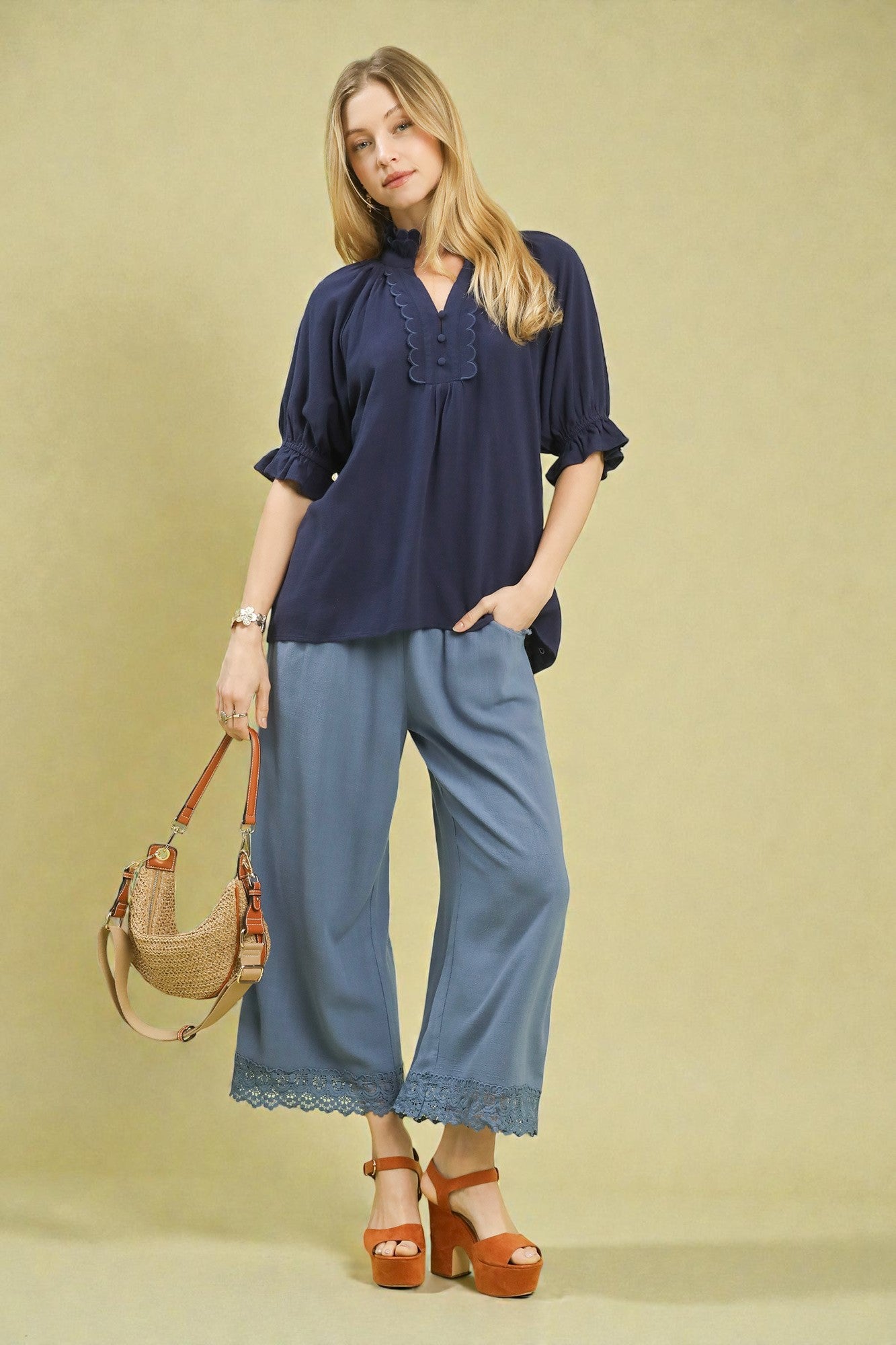 Woman wearing a navy blouse and blue pants with a beige handbag on a beige background