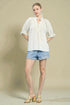 Woman wearing a white blouse and denim shorts against a beige background