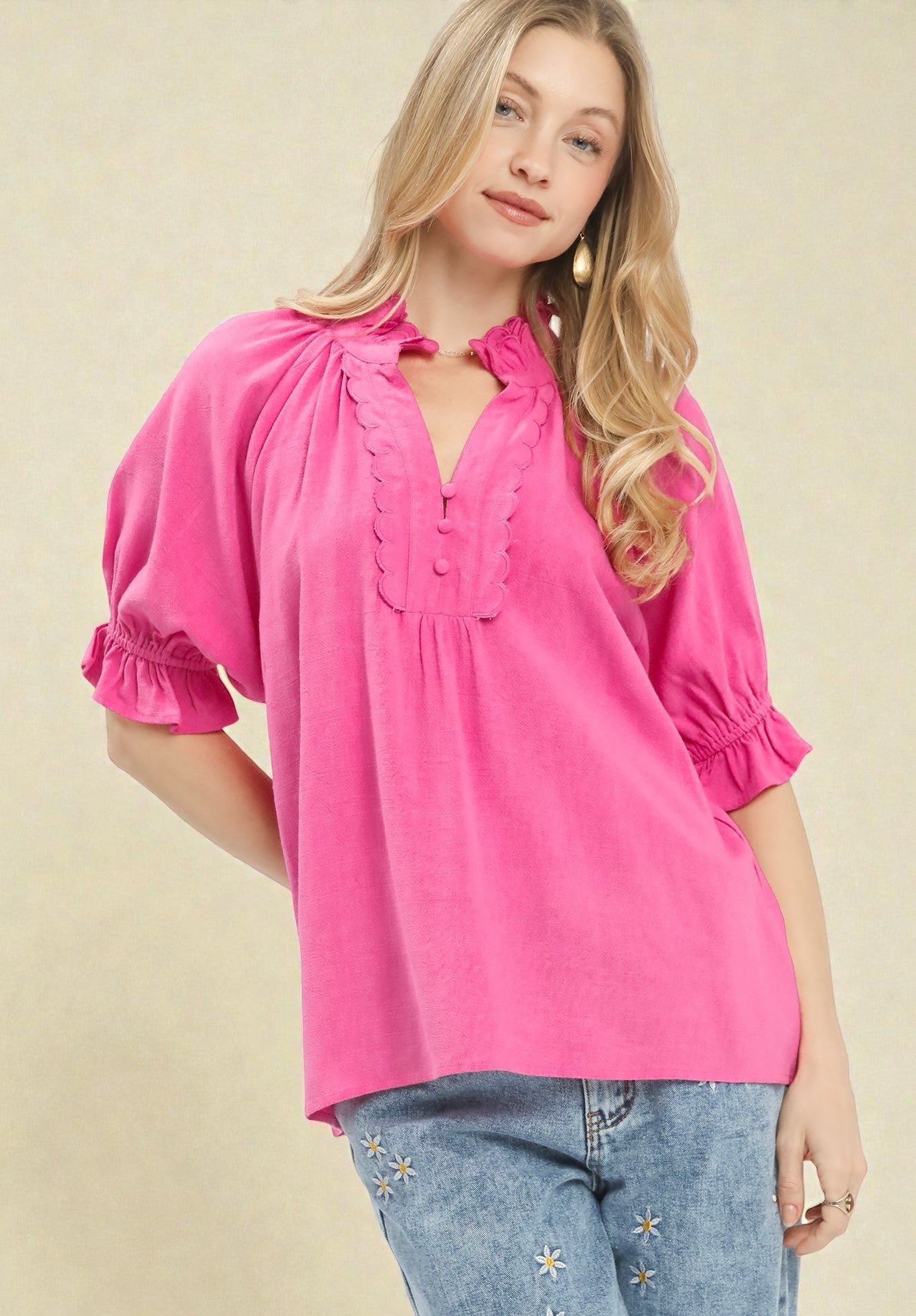 Woman wearing a bright pink blouse with ruffled sleeves on a beige background