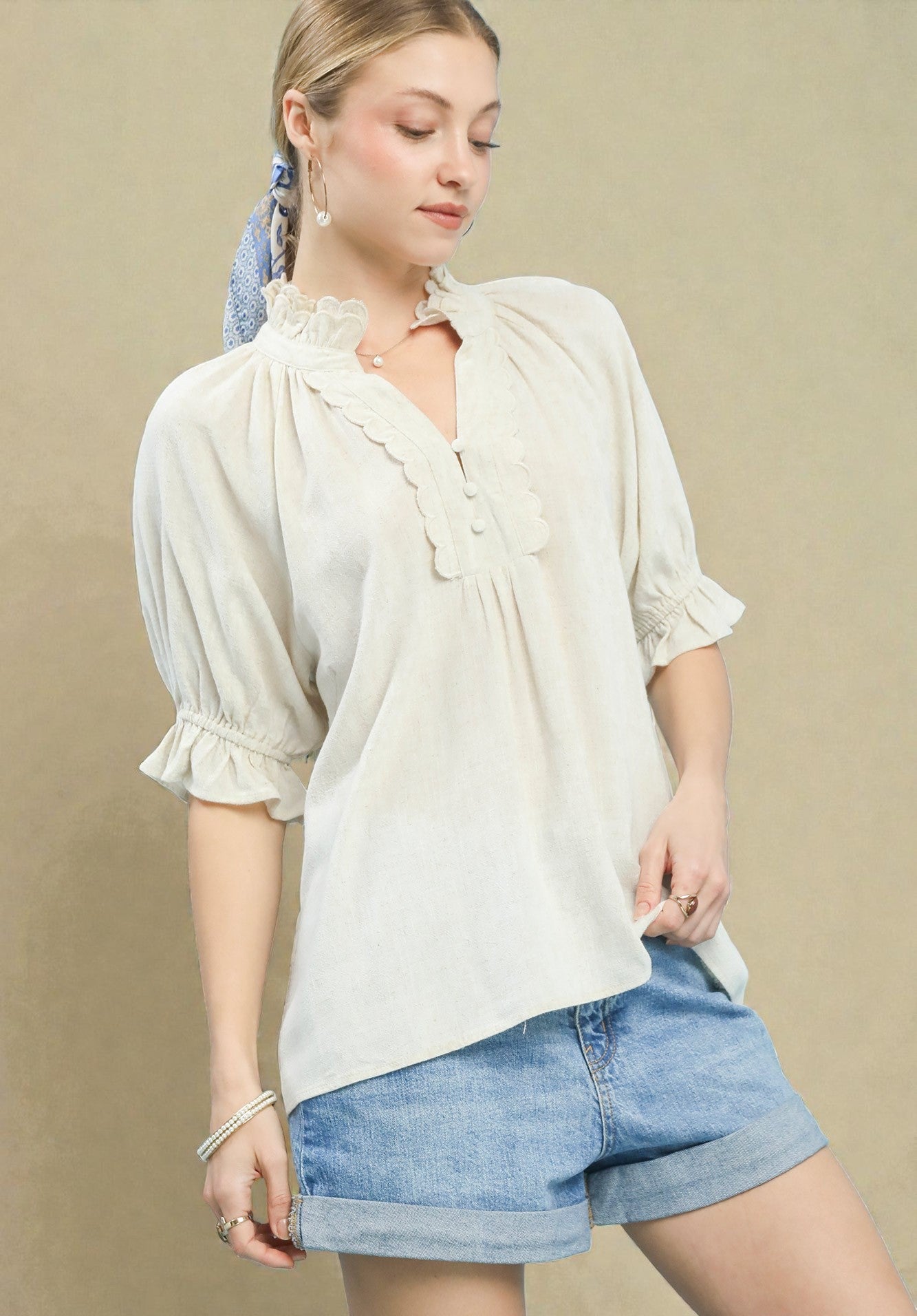 Woman wearing a light-colored blouse and denim shorts on a beige background