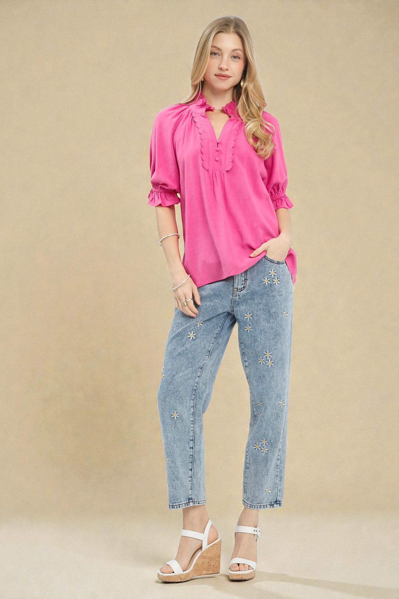 Woman wearing a bright pink blouse and light blue jeans against a beige background