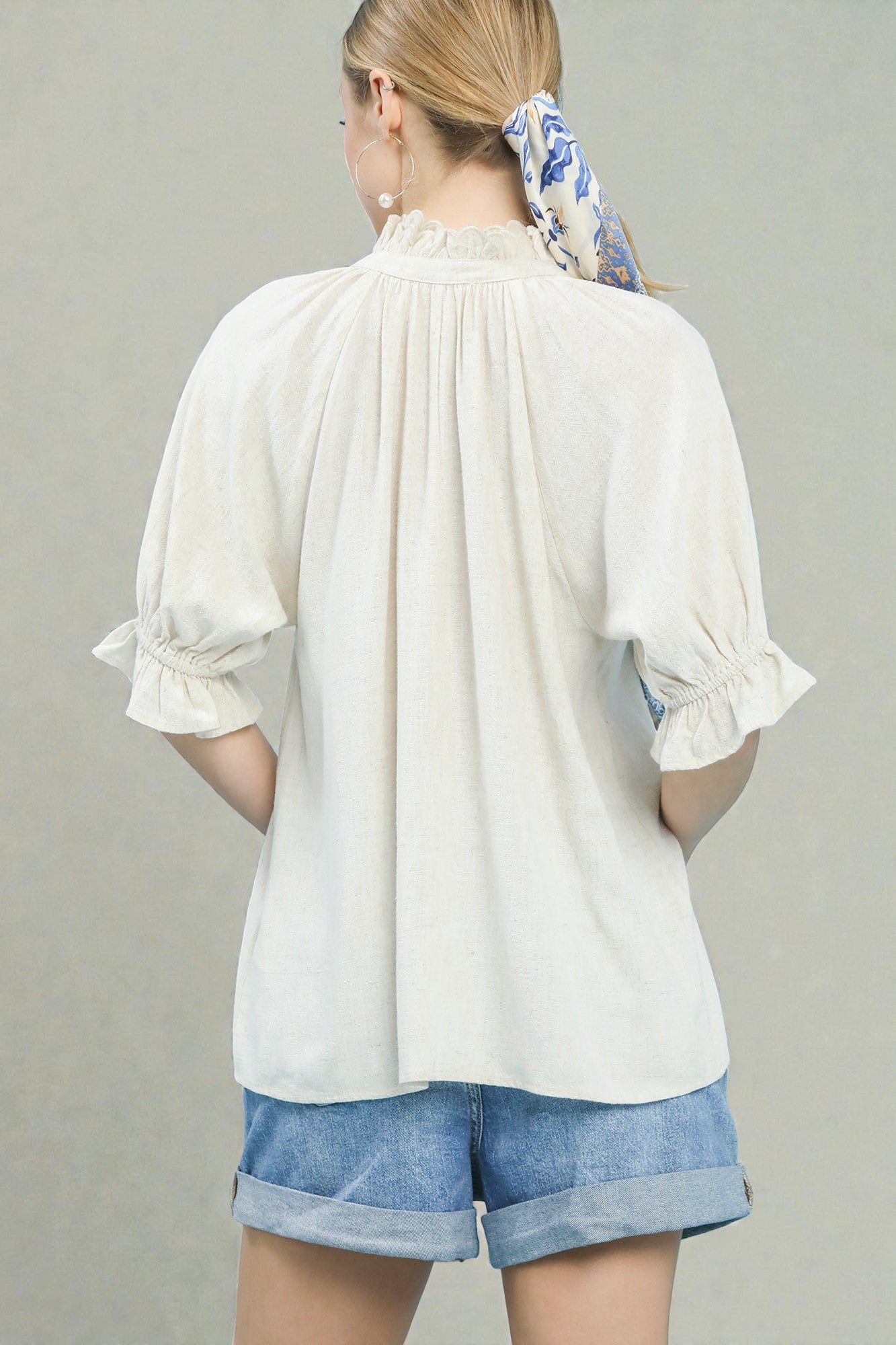 Woman wearing a white blouse and denim shorts with a gray background