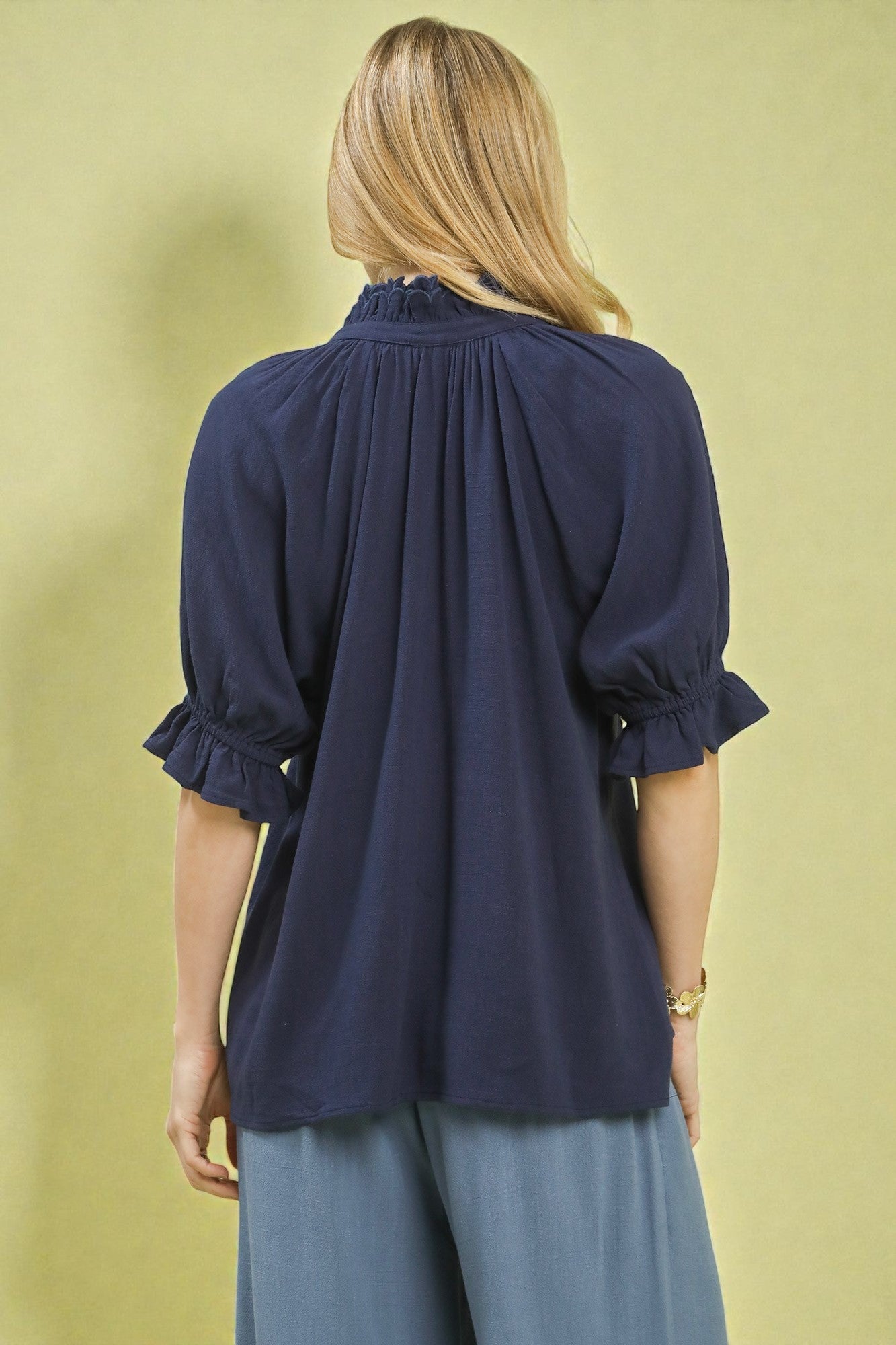 Navy blue blouse with ruffled sleeves worn by a person on a beige background