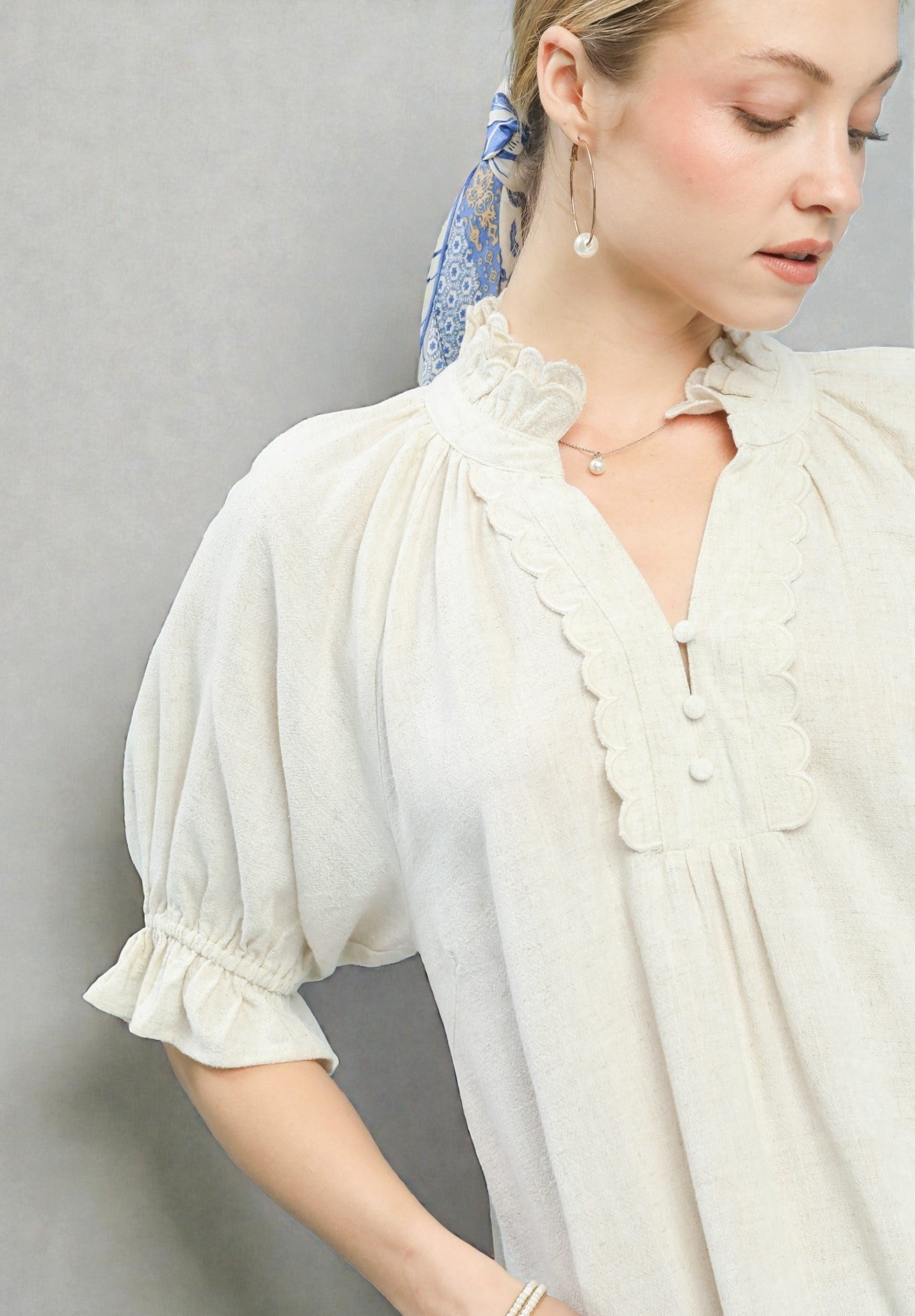 Woman wearing a white blouse with ruffled details against a gray background