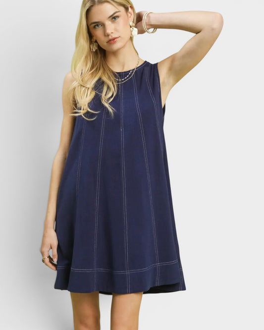 Woman wearing a navy blue sleeveless dress against a light gray background