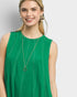 Woman wearing a green sleeveless top with a necklace on a plain background