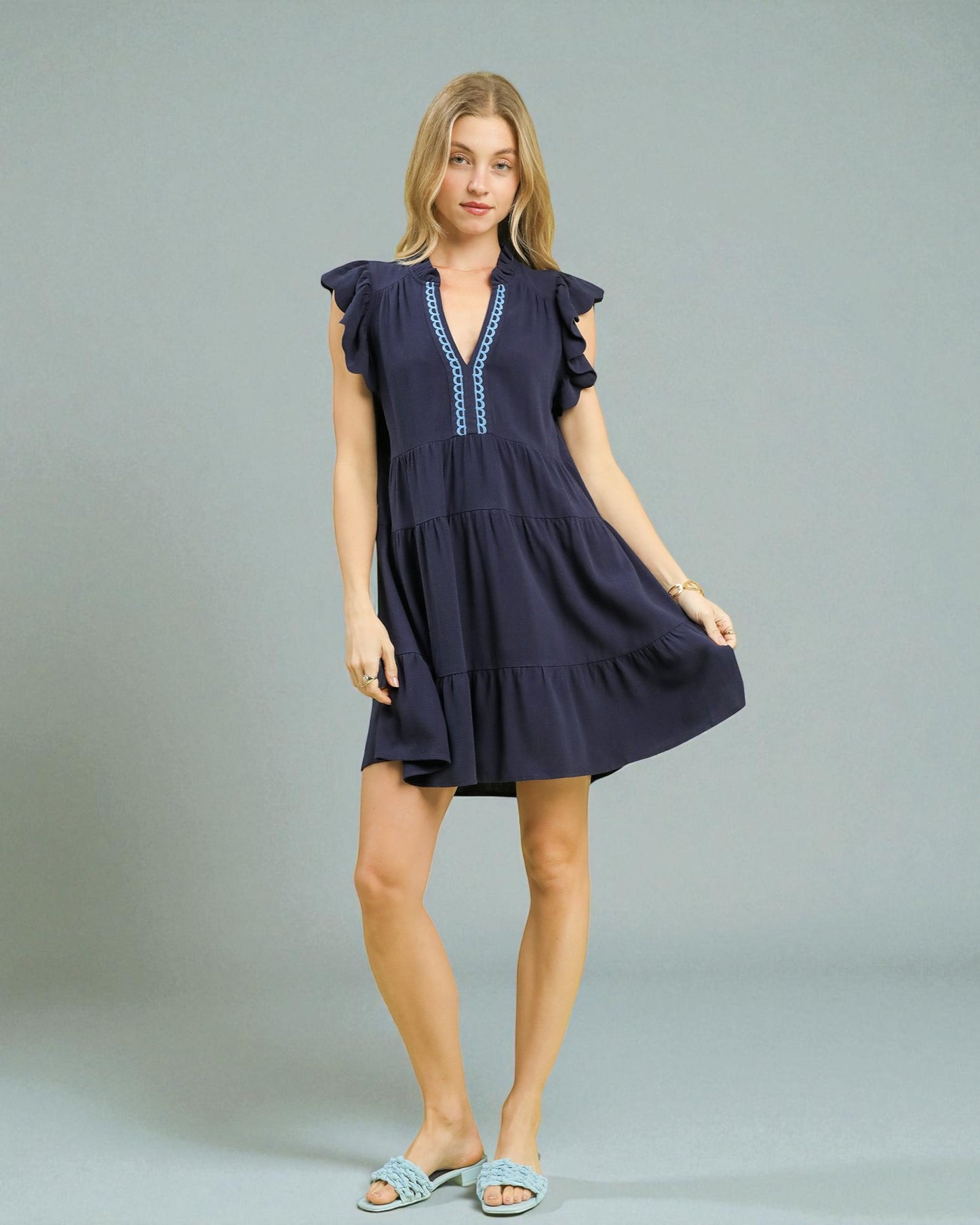 Woman wearing a navy blue dress with ruffled sleeves on a gray background