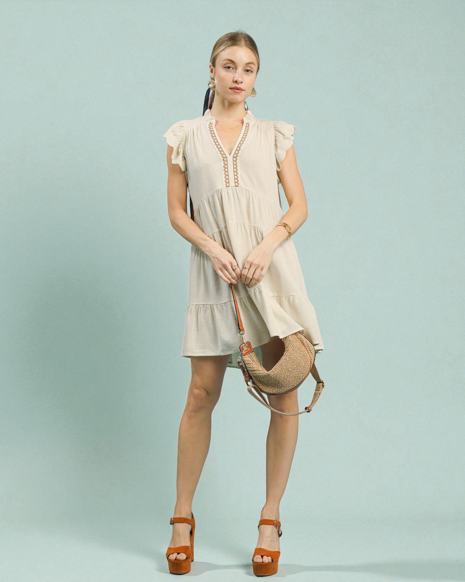 Woman wearing a beige dress holding a woven bag against a light blue background