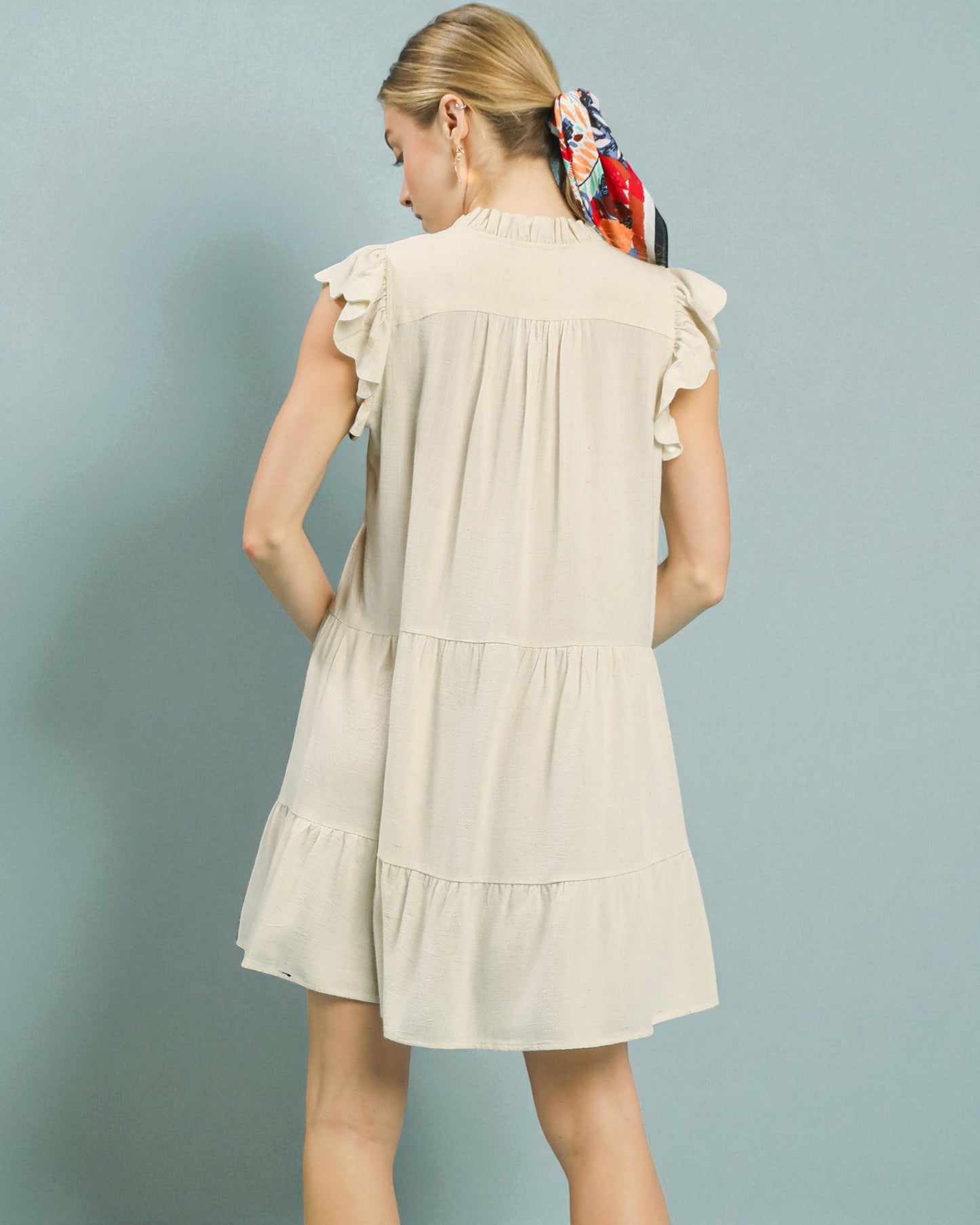 Woman wearing a beige dress with ruffled sleeves against a light blue background