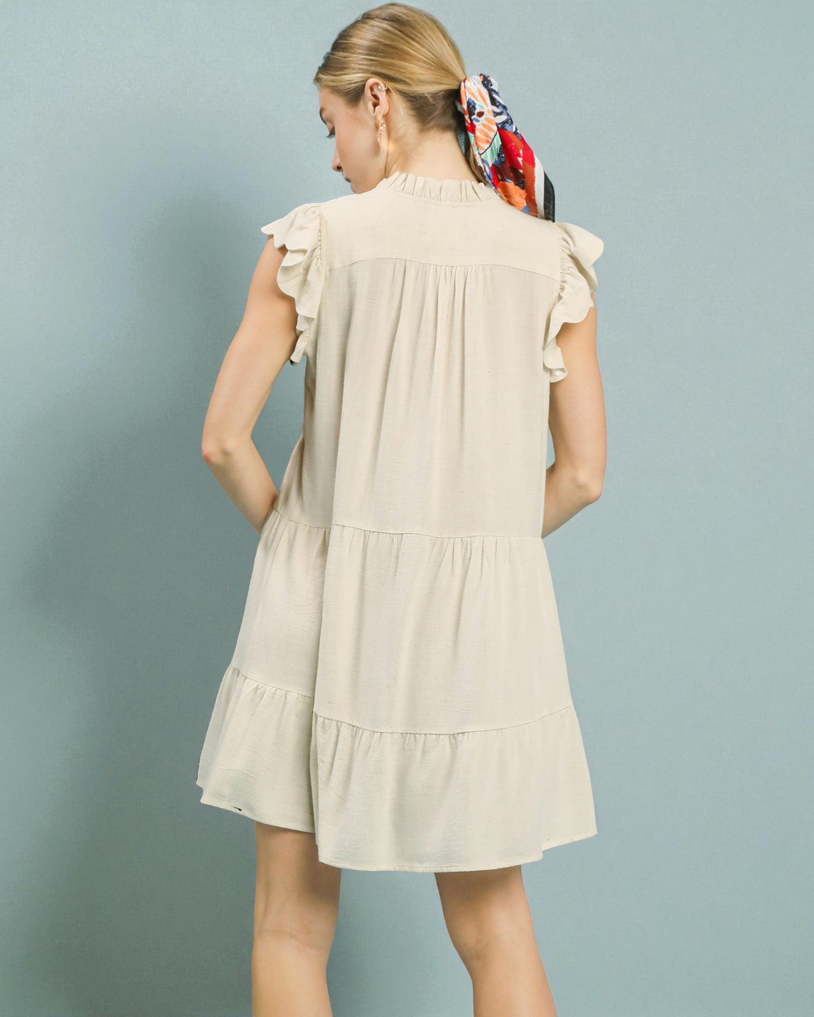 Woman wearing a beige dress with ruffled sleeves against a light blue background