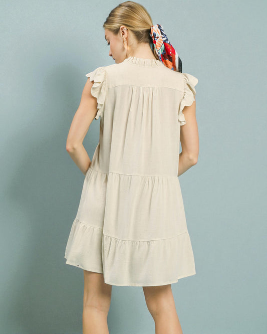 Woman wearing a beige dress with ruffled sleeves against a light blue background