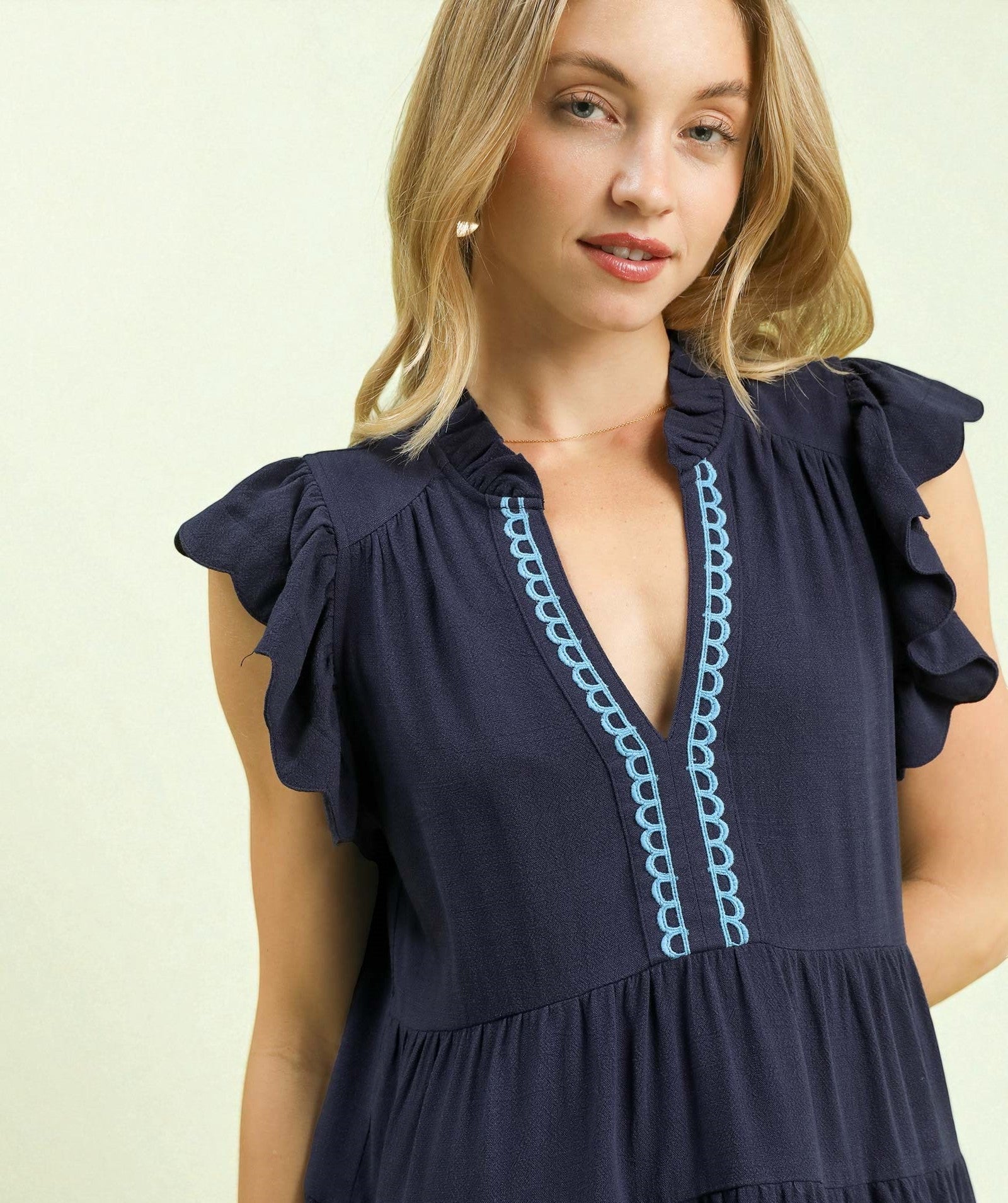 Woman wearing a navy dress with blue embroidery on a light background