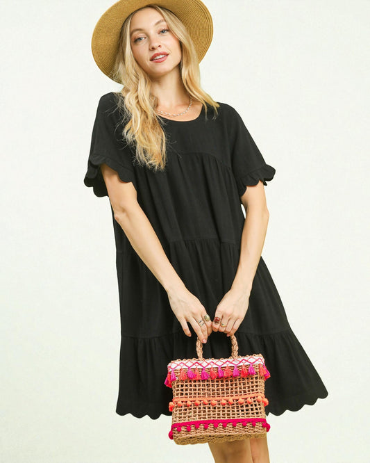 Woman in a black dress holding a colorful woven bag on a white background