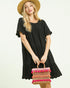 Woman in a black dress holding a colorful woven bag on a white background