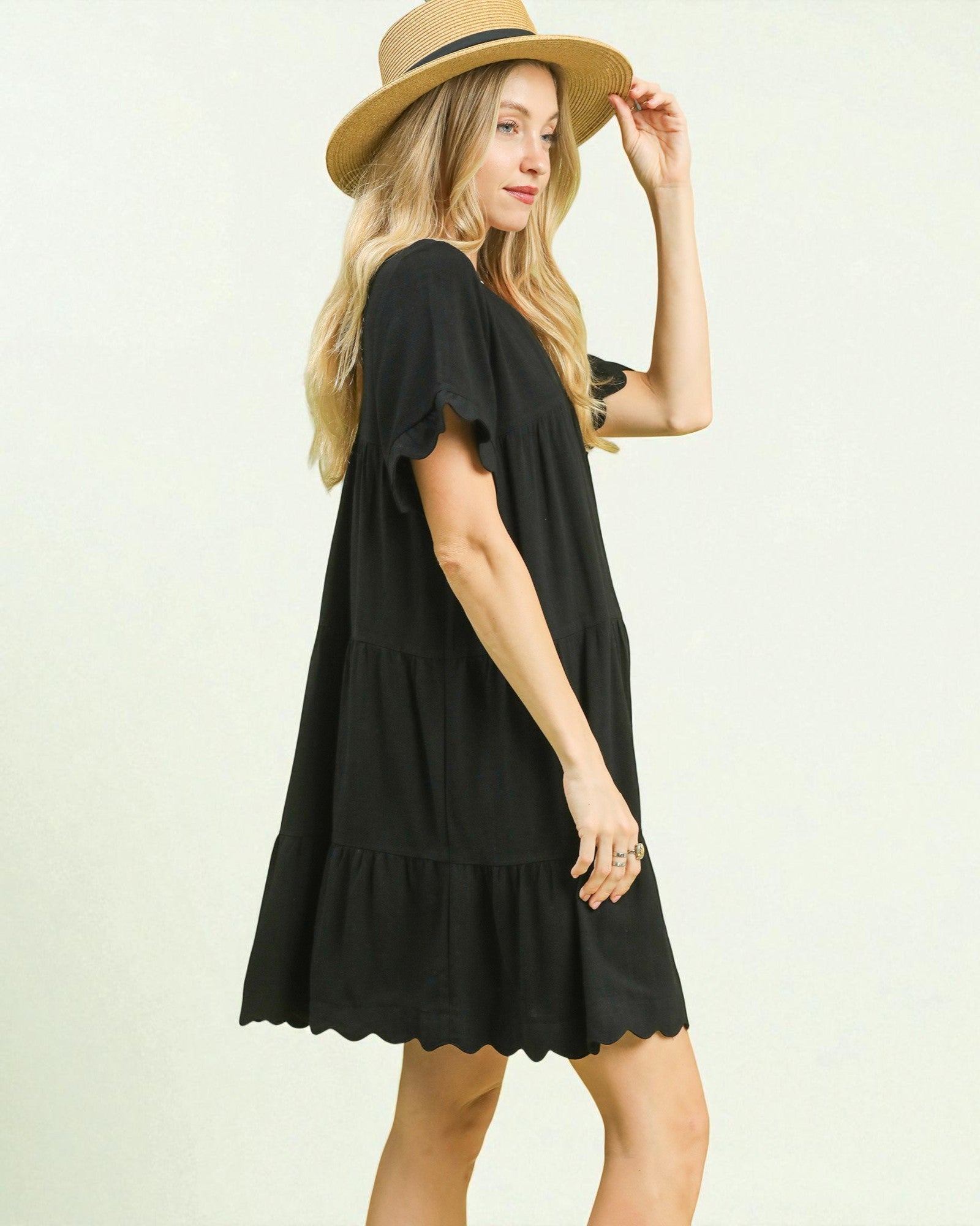 Woman wearing a black dress and beige hat on a light background