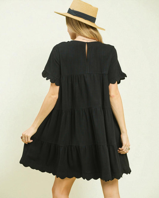 Woman wearing a black dress with ruffled sleeves and hem, standing against a plain background.