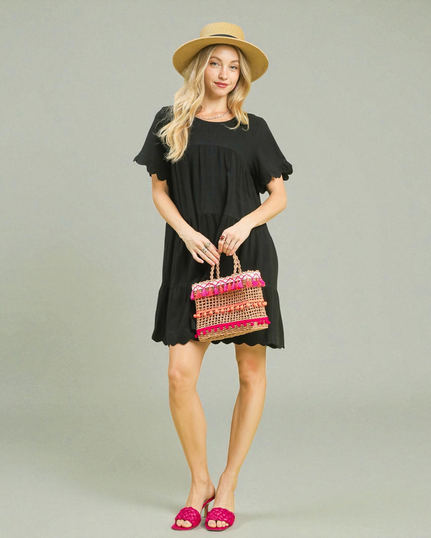 Woman in a black dress holding a colorful handbag against a plain background