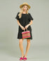 Woman in a black dress holding a colorful handbag against a plain background