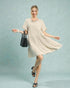 Woman in a beige dress holding a black handbag against a light blue background
