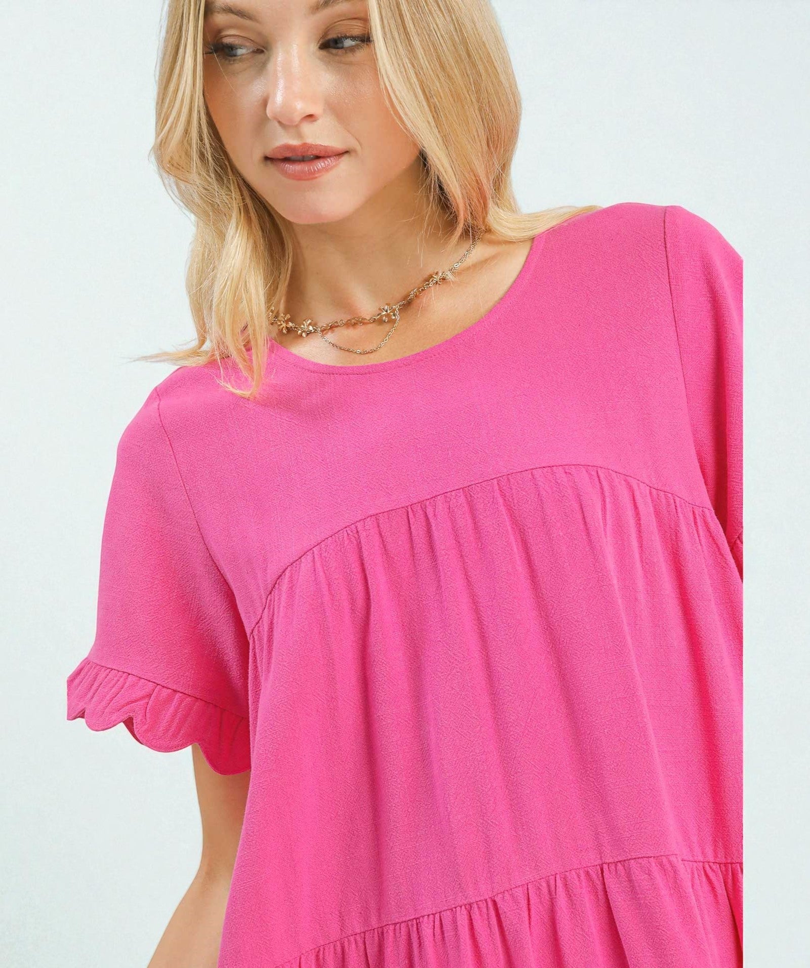 Woman wearing a pink dress with scalloped sleeves on a white background